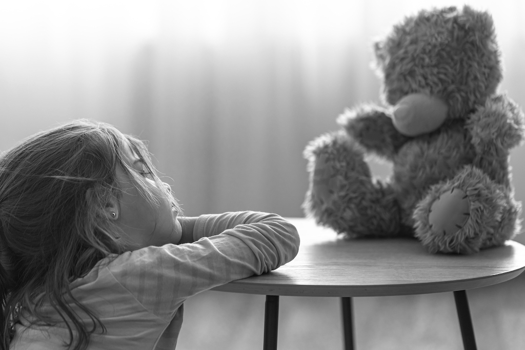 Sad little girl playing with a teddy bear.
